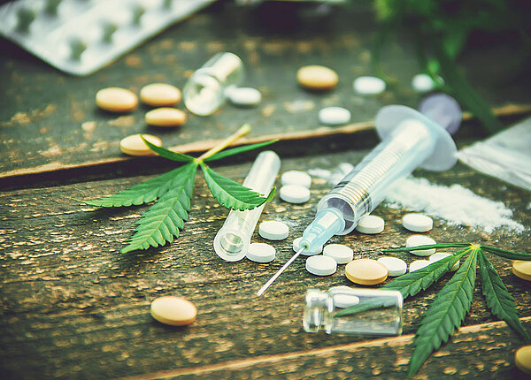 Auswahl Betäubungsmittel wie Pillen, Spritze mit Heroin, Kokain, Cannabisblätter auf einem Holztisch 