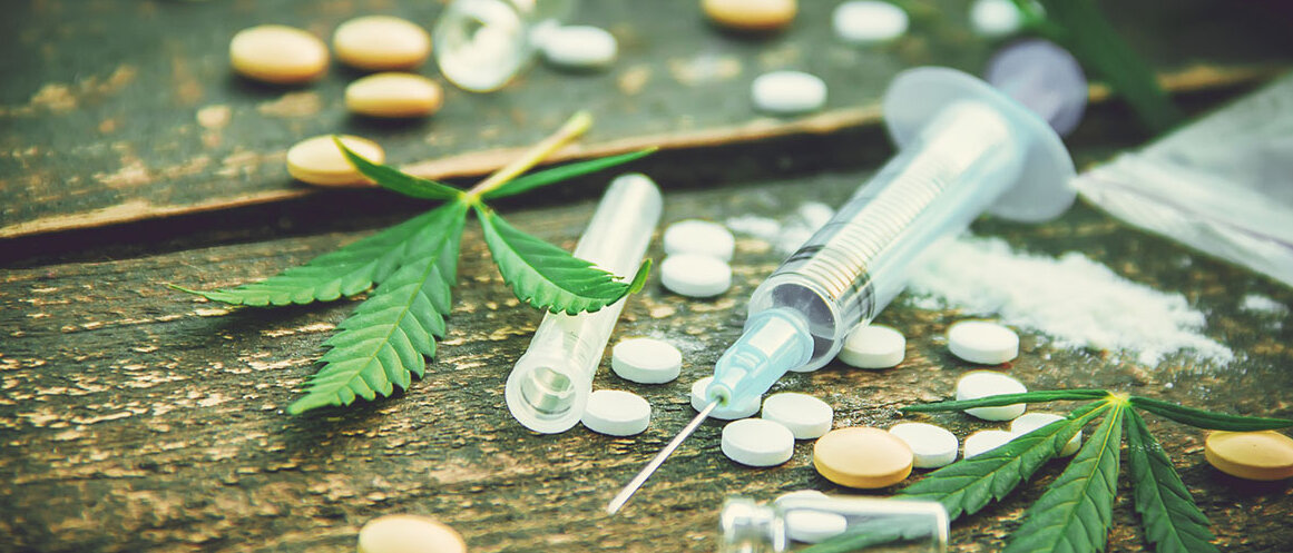 Auswahl Betäubungsmittel wie Pillen, Spritze mit Heroin, Kokain, Cannabisblätter auf einem Holztisch 