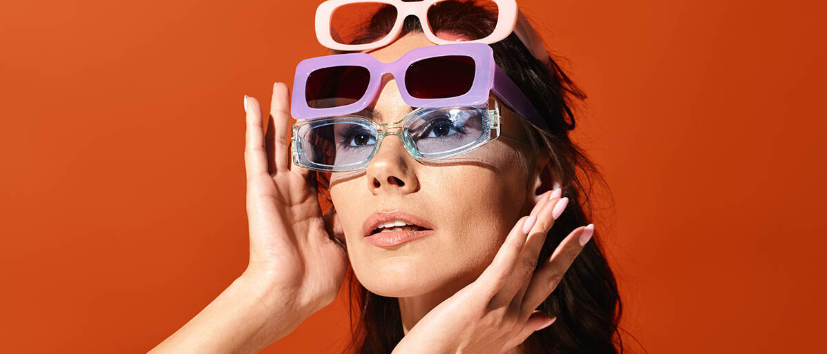 Sonnenbrille kaufen: UV-Schutz, Blendschutz, Farbe der GlĂ€ser und GröĂe richtig wĂ€hlen Eine junge Frau hat drei verschiedene Sonnenbrillen in unterschiedlichen Farben auf.