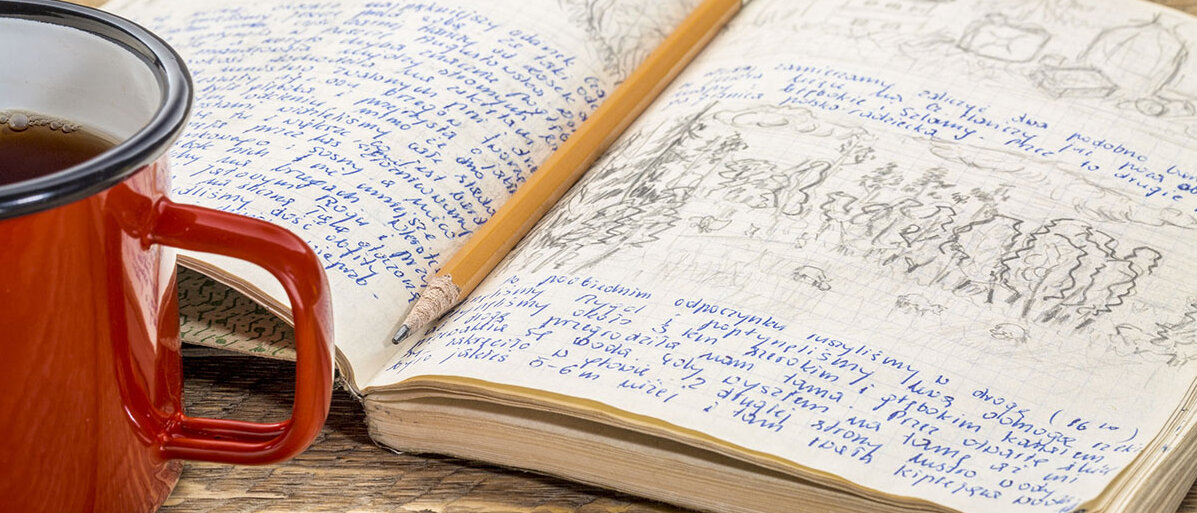 Offenes Notizbuch mit Notizen, in der Mitte liegt ein Bleistift und nebendran steht eine rote Tasse mit Kaffee