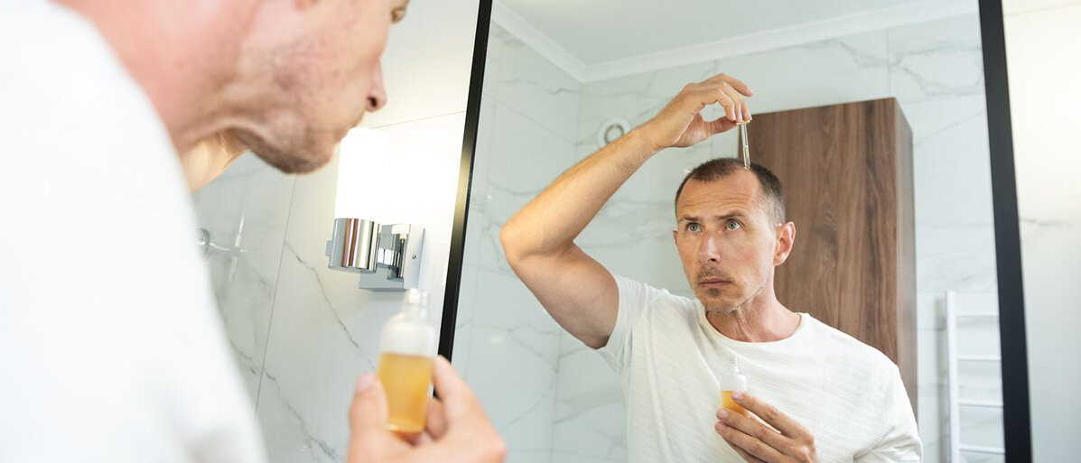 Nebenwirkungen von Minoxidil Mann vor Spiegel trÀgt Minoxidil auf