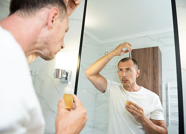 Nebenwirkungen von Minoxidil Mann vor Spiegel trägt Minoxidil auf