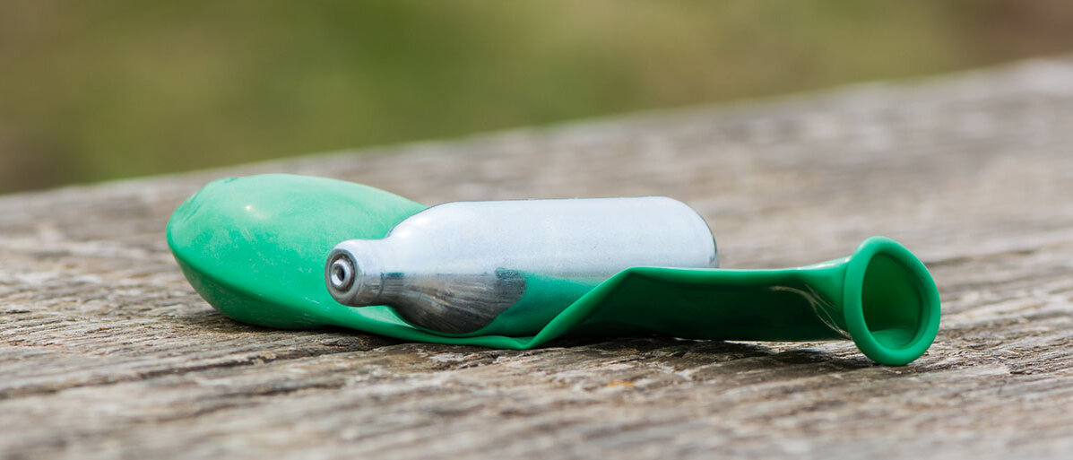 Lachgas-Kartusche mit grünem, nichtaufgeblasenem Luftballon auf Holzbank