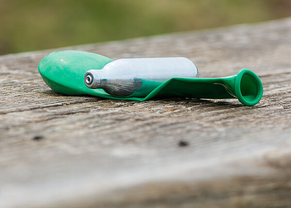 Lachgas-Kartusche mit grünem, nichtaufgeblasenem Luftballon auf Holzbank