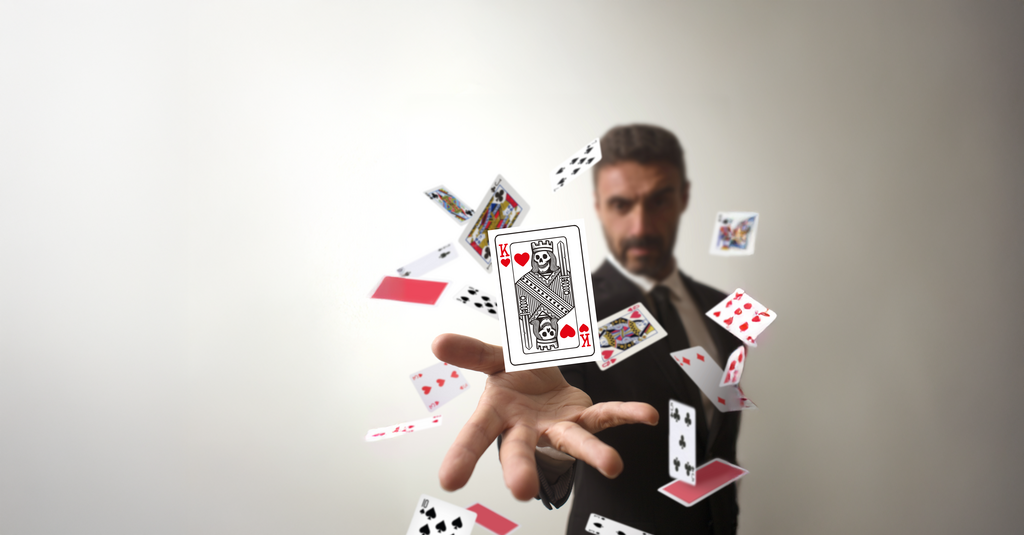 Ein Mann macht einen Kartentrick, dabei wirbelt er Spielkarten durch die Luft. Dem Betrachter zugewandt ist der Herzkönig. Auf dem Kartenbild hat der Herzkönig kein Gesicht, sondern einen Totenschädel. 