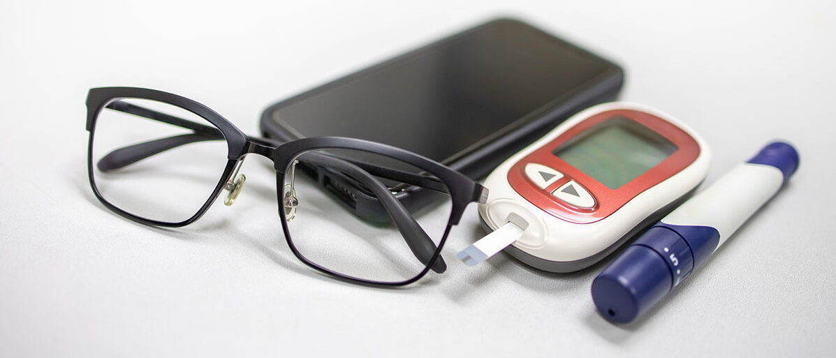 Ein Smartphone, ein Blutzuckermessgerät, eine Stechhilfe und eine Brille