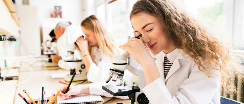Mehrere junge Frauen schauen durch Mikroskope und machen sich Notizen