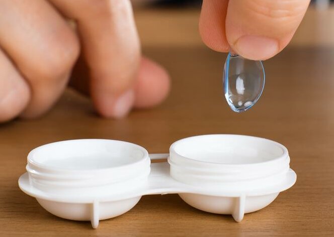 Jemand legt eine Kontaktlinse in eine Transportdose.