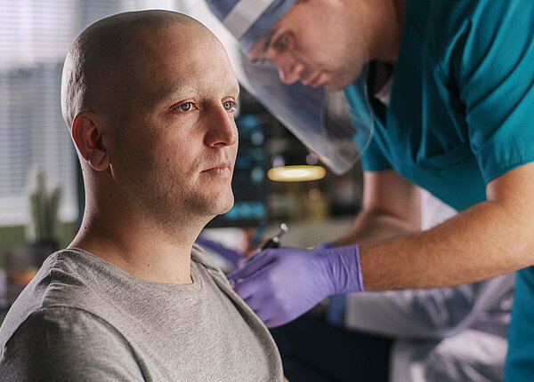 Ein Krankenpfleger oder Arzt mit Gesichtsvisier impft einen Mann mit Glatze.