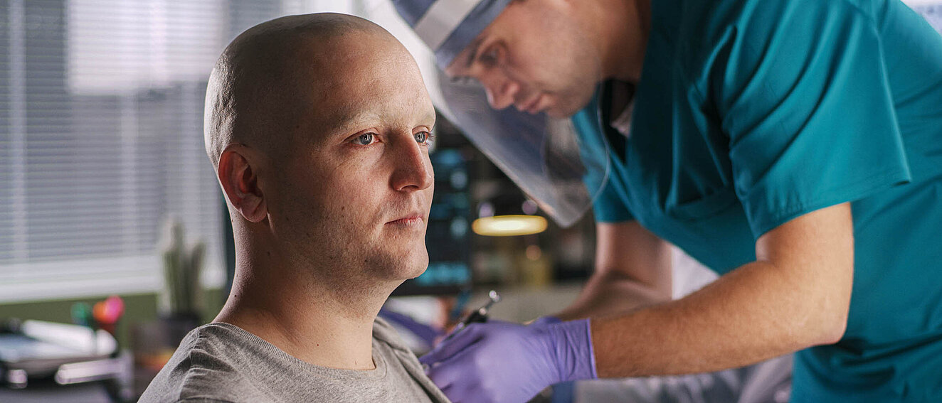 Ein Krankenpfleger oder Arzt mit Gesichtsvisier impft einen Mann mit Glatze.