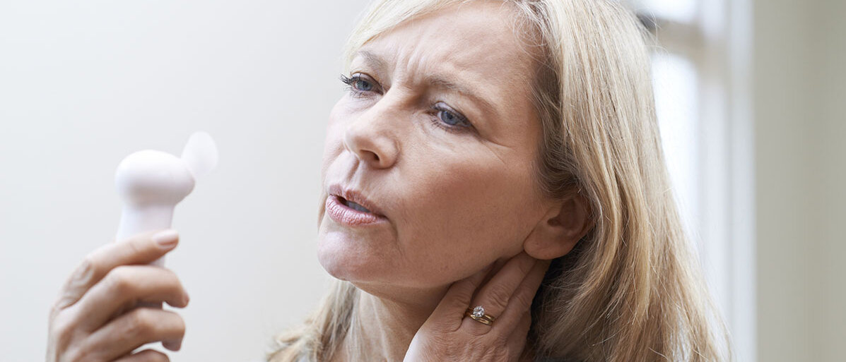 Symptome während der Wechseljahre lindern Ältere Frau hält sich Miniventilator vor das Gesicht