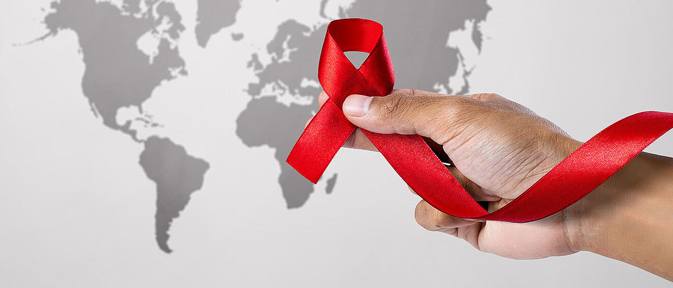 Bessere Teststrategien gegen HIV Eine Hand hält eine rote Schleife vor einer Weltkarte