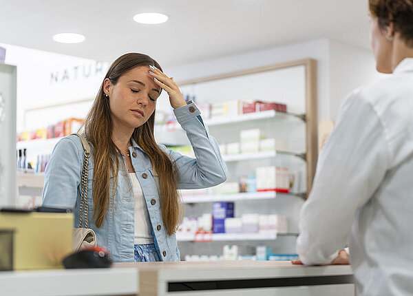 Safe Space Apotheken in Berlin und Brandenburg sind Anlaufstellen für Jugendliche mit Problemen und vermitteln Hilfe – zum Beispiel zum Thema Mental Health. Eine Jugendliche lässt sich am HV-Tisch beraten. Sie hat die Augen geschlossen, fasst sich an die Stirn und hat einen betrübten Gesichtsausdruck.