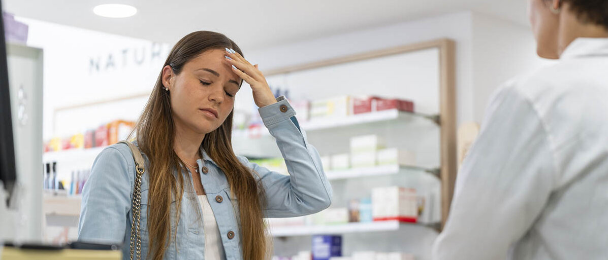 Safe Space Apotheken in Berlin und Brandenburg sind Anlaufstellen für Jugendliche mit Problemen und vermitteln Hilfe – zum Beispiel zum Thema Mental Health. Eine Jugendliche lässt sich am HV-Tisch beraten. Sie hat die Augen geschlossen, fasst sich an die Stirn und hat einen betrübten Gesichtsausdruck.