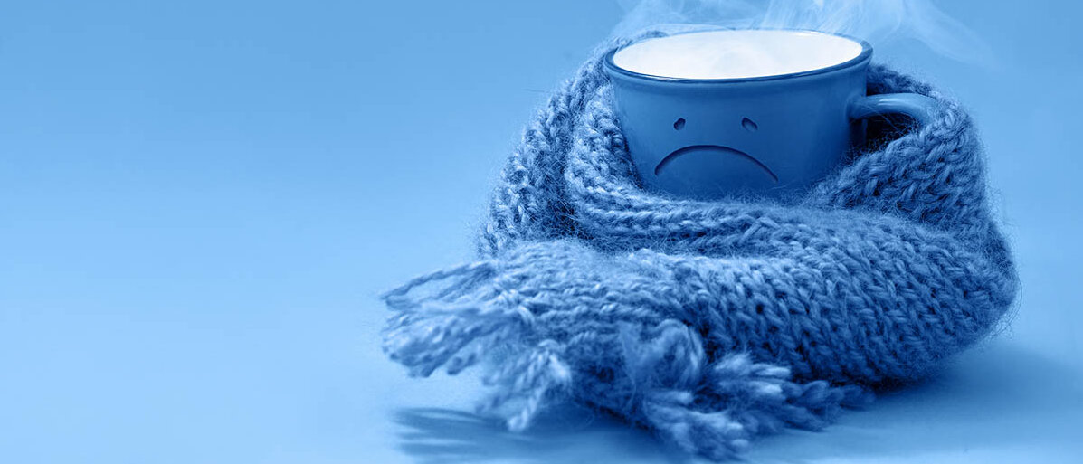 Ursache fĂĽr SchĂĽttelfrost: Warum wir bei Fieber frieren eine Tasse mit dampfendem Inhalt hat ein motziges Gesicht und einen Schal umgewickelt