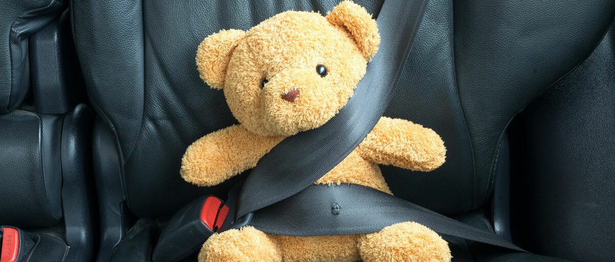 Auf der Rückbank eines Autos ist ein Teddybär mit Dreipunktgurt angeschnallt.