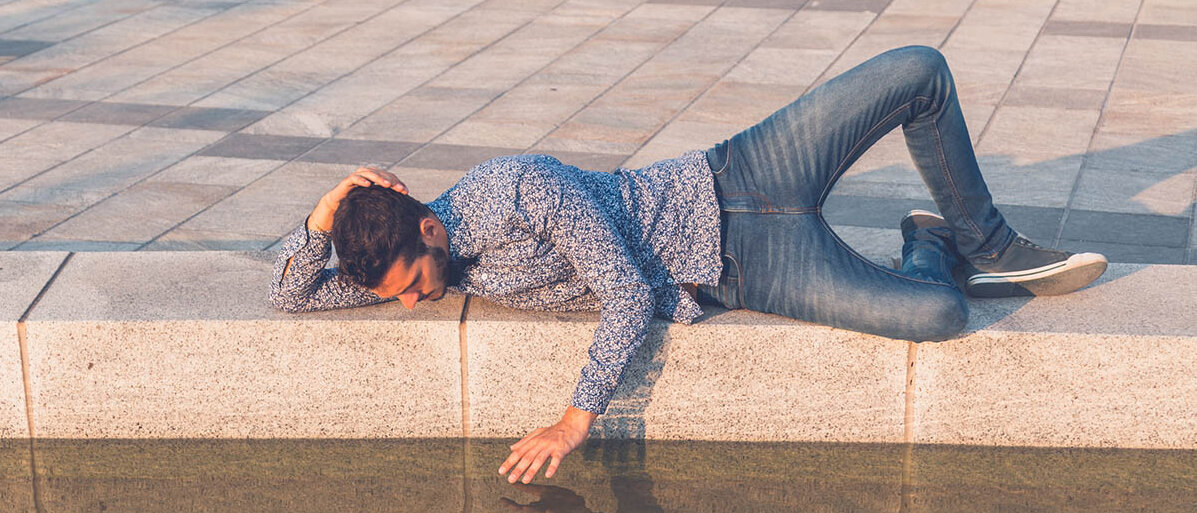 Ein Mann liegt am Rand eines Wasserbeckens und streichelt sein eigenes Spiegelbild.