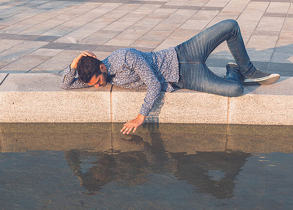 Ein Mann liegt am Rand eines Wasserbeckens und streichelt sein eigenes Spiegelbild.