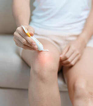 Eine Frau trägt eine gelartige Creme aus einer Tube auf ihr Knie auf.