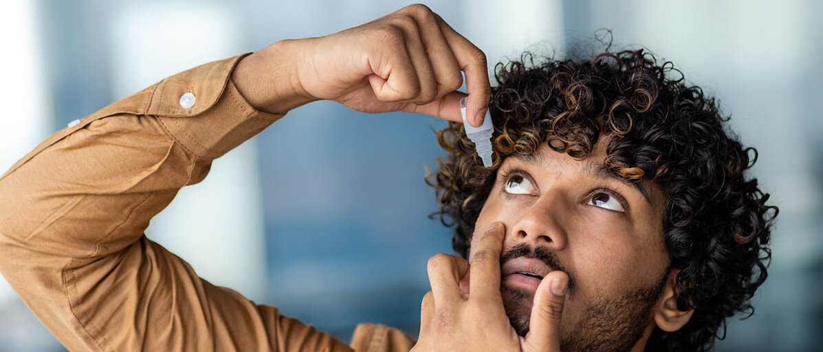 Allergie Augentropfen gegen Heuschnupfen im Vergleich Ein junger Mann versucht, sich Augentropfen aus einem MehrdosenbehÀltnis ins Auge zu tropfen.