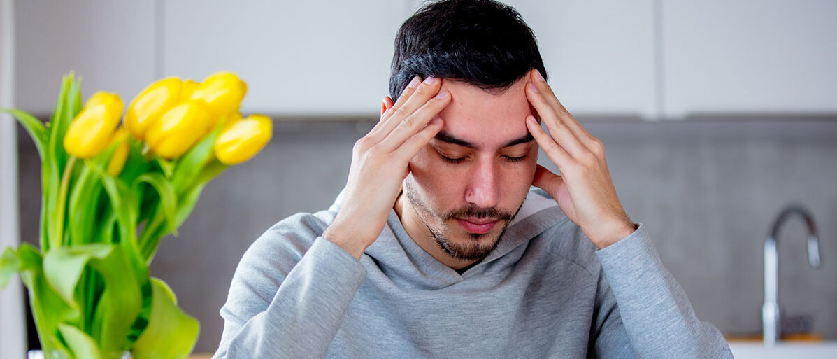 Tipps gegen den Kater am Morgen danach Mann sitzt am Tisch mit Tasse Kaffee, hält sich den Kopf
