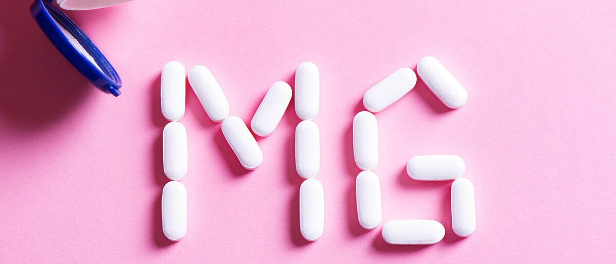Flatlay: Aus einer Tablettendose sind weiße Tabletten herausgefallen und bilden die Buchstaben „Mg“.
