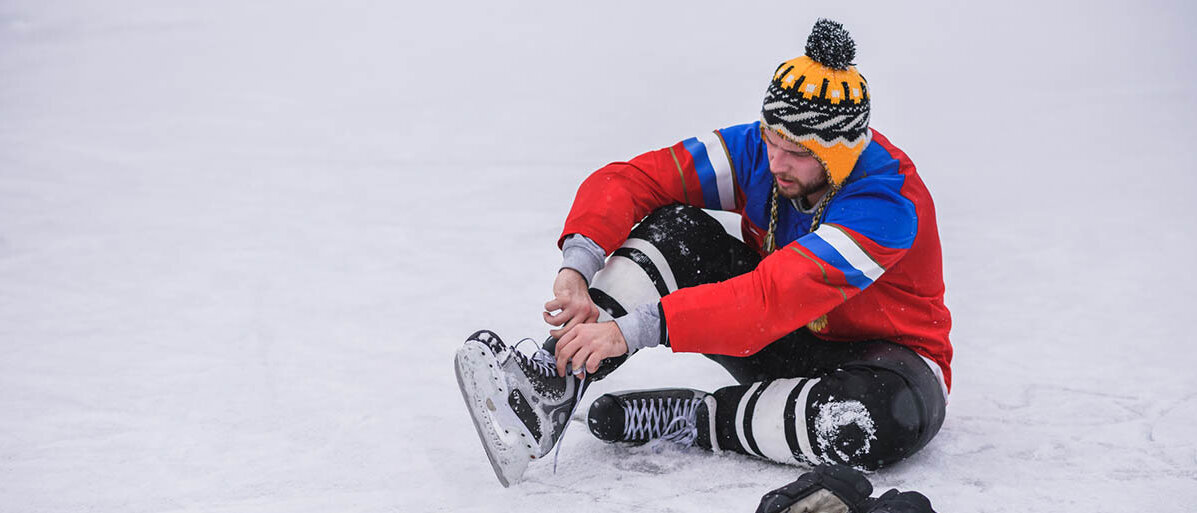 Ein Eishockeyspieler sitzt auf dem Eis, hat ein Bein aufgestellt und schnürt seinen Schlittschuh.