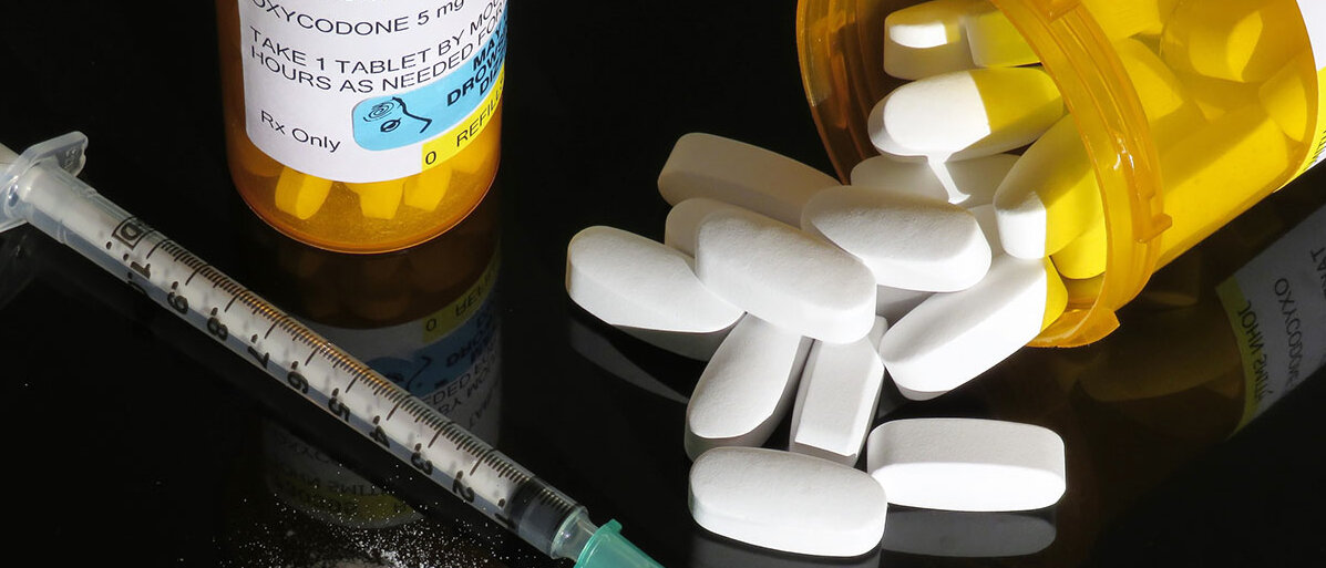 Eine Tablettendose mit Oxycodon, wie sie in den USA üblich ist, daneben eine Spritze und ein weißes Pulver