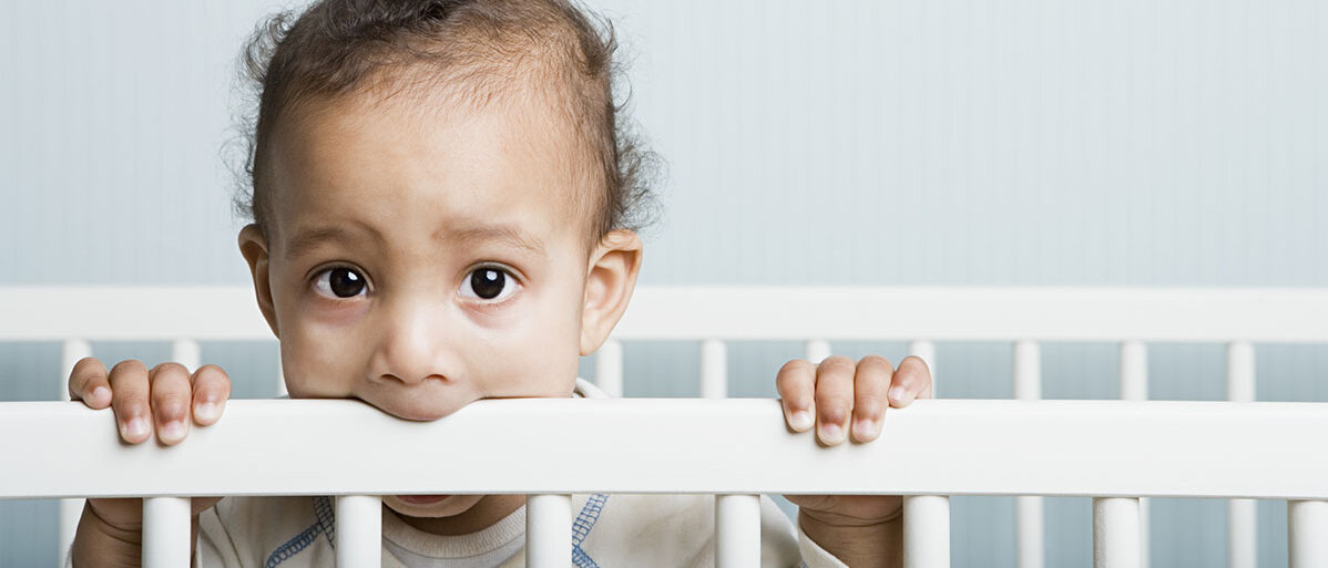 Kleiner Junge beißt auf den Rahmen seines Kinderbettes.