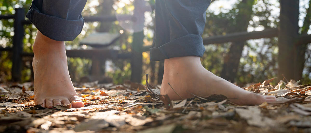 Barfußlaufen: Vorteile und Tipps Jemand läuft barfuß über einen Weg voller Herbstlaub.