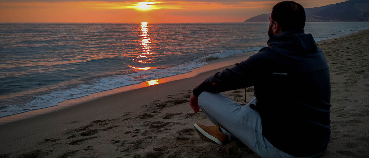 Mann sitze am Strand und blickt auf den Sonnenuntergang