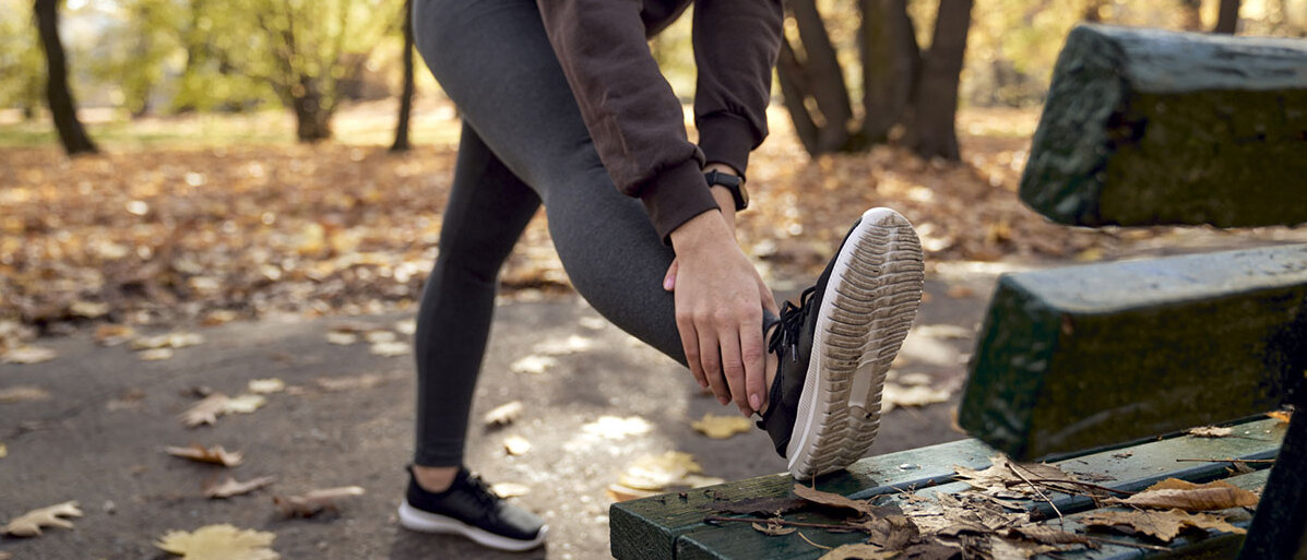 Frau dehnt sich nach dem Joggen im herbstlichen Wald