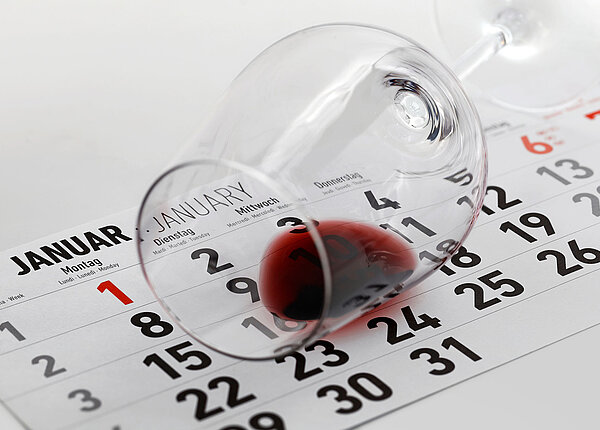 Januarseite im Kalender darüber ein umgestoßenes Weinglas mit Rotwein-Rest