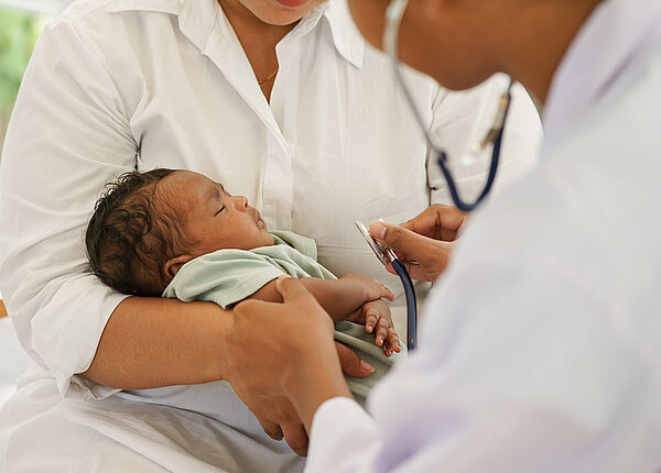 Neugeborenes Kind auf dem Arm der Mutter wird vom Arzt untersucht