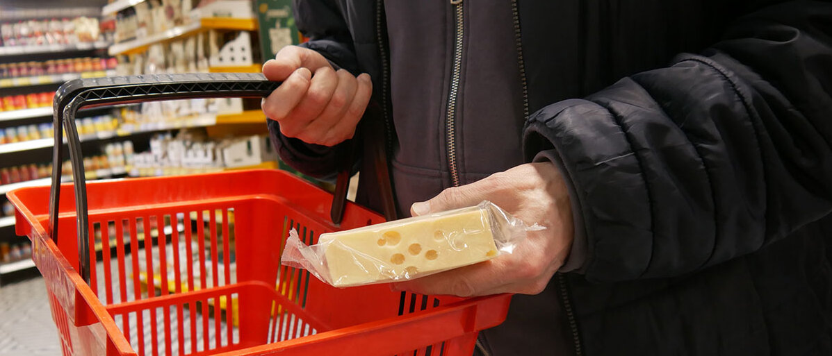 Mann packt eingeschweißten Käse in roten Einkaufskorb 