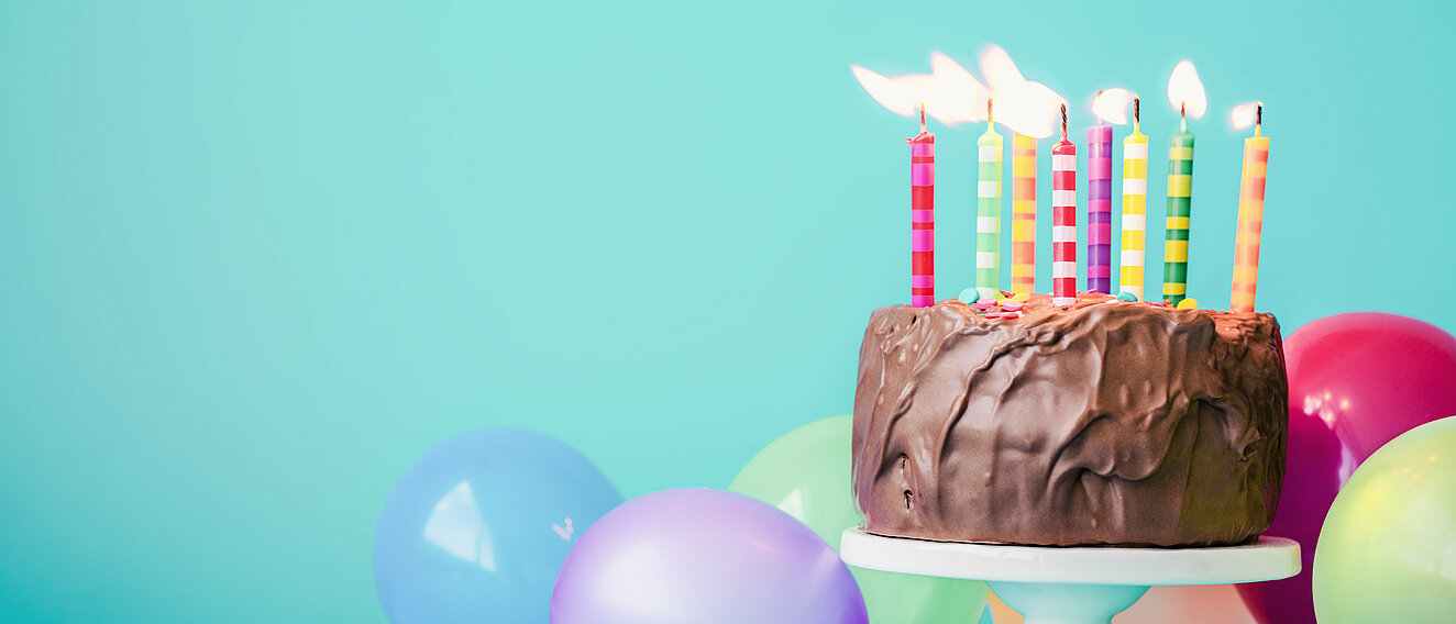 Geburtstag Ein Schokokuchen mit brennenden Kerzen und bunte Ballons