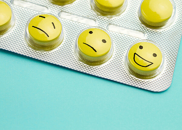 Ein Blister mit gelben Tabletten. Auf den Tabletten sind unterschiedliche Smileys aufgemalt