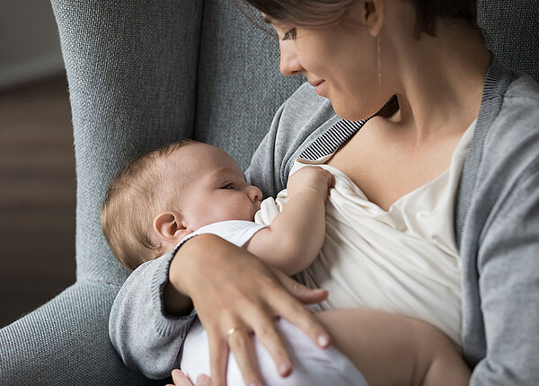 : Frau sitzt im Sessel und stillt ihr Baby