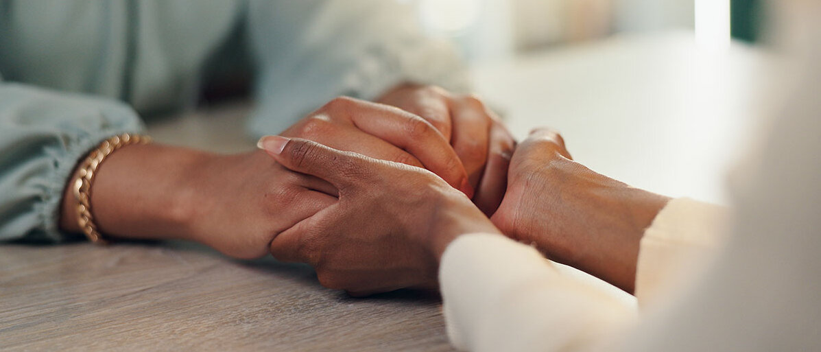 Unterstützung für Menschen mit Depression Zwei afrodeutsche Frauen halten sich tröstend die Hände.