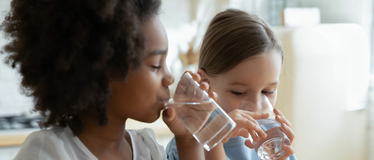 Zwei kleine Mädchen trinken jeweils ein Glas Wasser