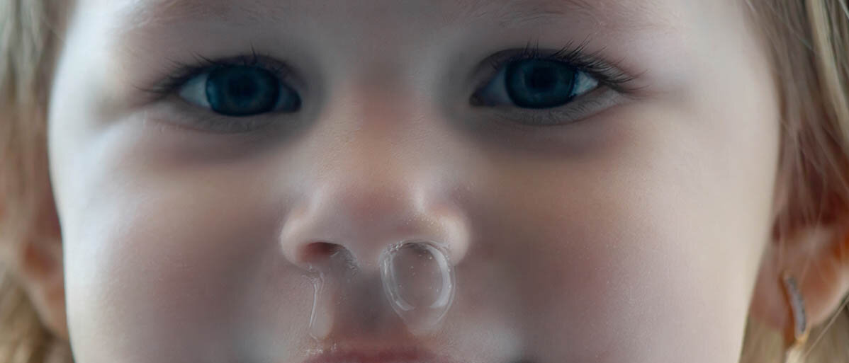 Kind krank durch Kita: Warum Kleinkinder viele Infekte durchmachen Einem Kleinkind blubbert Schnupfen aus der Nase.