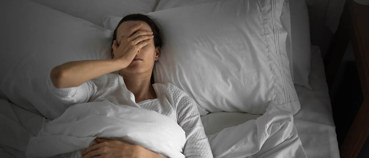 Eine Frau liegt schlaflos im Bett und hält sich die Hand auf das Gesicht.