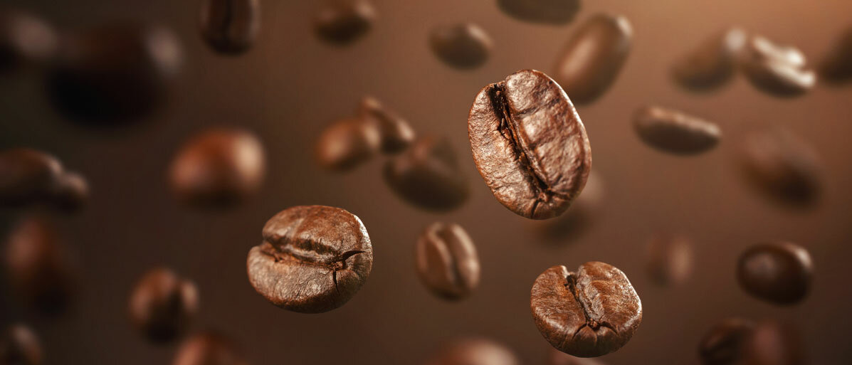 Einzelne Kaffeebohnen fallen auf dunklem Hintergrund