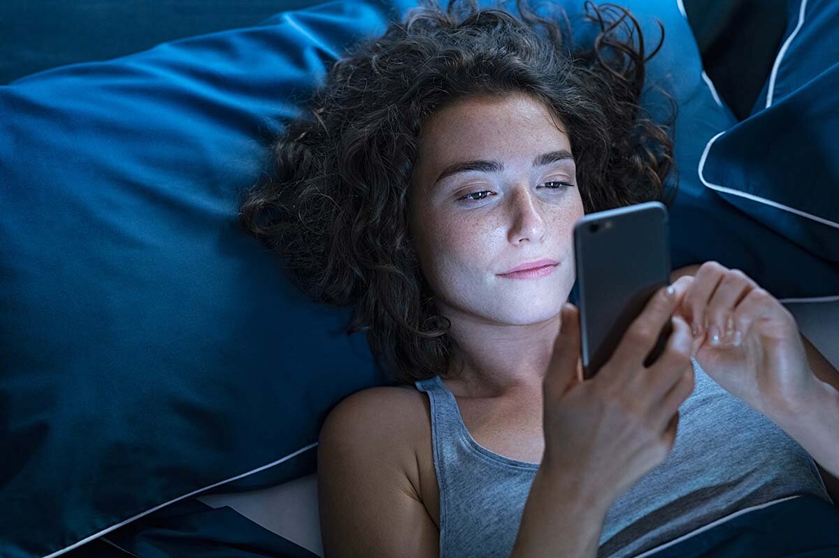 Frau liegt mit Smartphone im Bett.