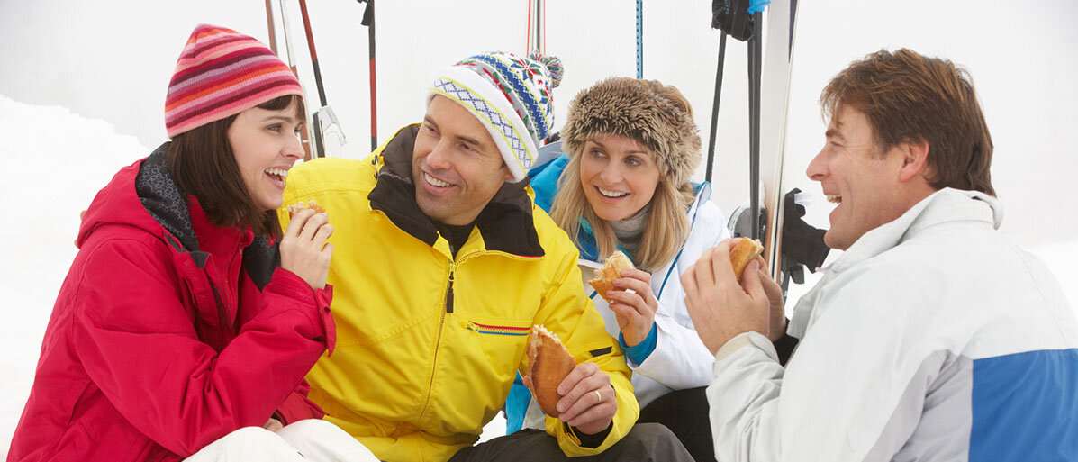 2 Frauen und 2 Männer sitzen im Schnee und Essen was