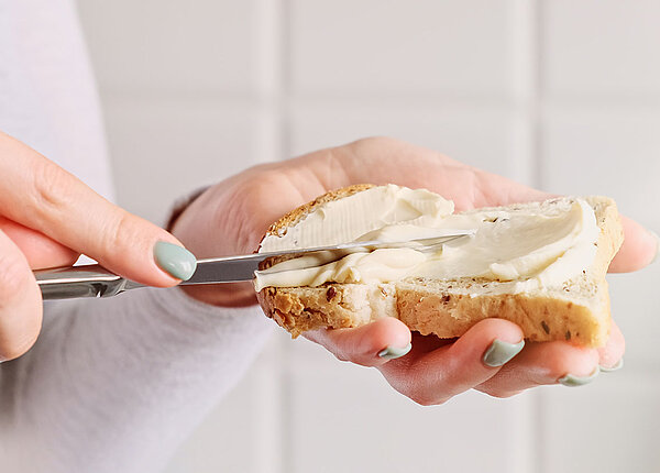 Butter oder Margarine? Frau bestreicht Brotscheibe mit Butter oder Margarine