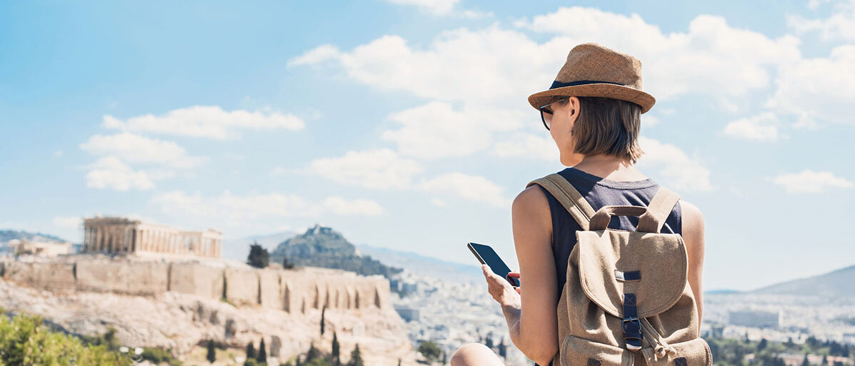 Digital Detox im Urlaub Frau von hinten mit Rucksack und Smartphone im Urlaub in Athen