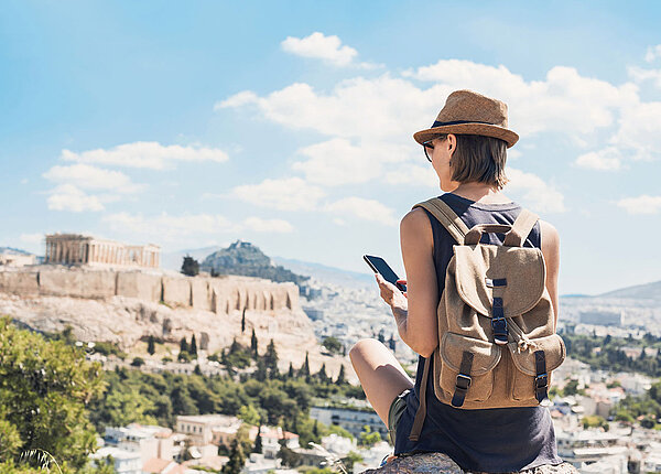 Digital Detox im Urlaub Frau von hinten mit Rucksack und Smartphone im Urlaub in Athen