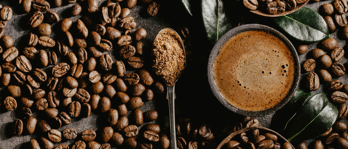 Eine Tasse Kaffee und ein Löffel Kaffeepulver inmitten von Kaffeebohnen
