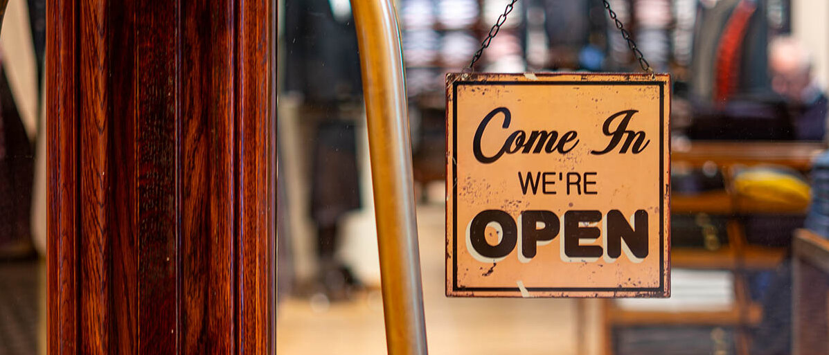 An einer alten Ladentür aus Holz hängt in einer Glasscheibe ein Schild: Come In, we’re open.